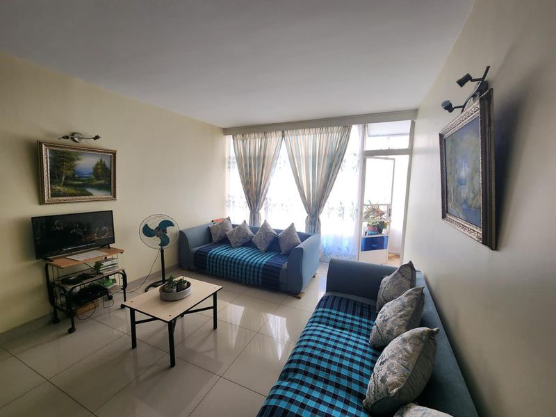 A bright living room featuring tiled flooring and direct access to an adjoining balcony through a sliding glass door.