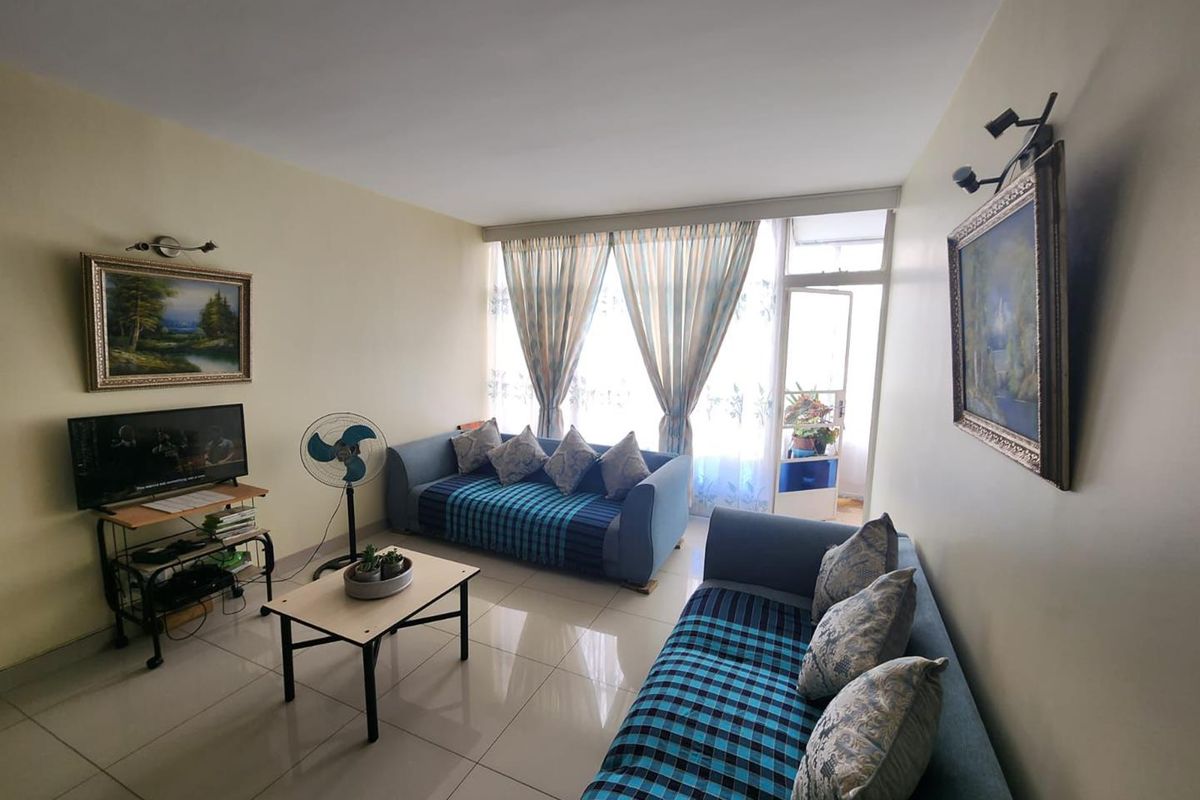 A bright living room featuring tiled flooring and direct access to an adjoining balcony through a sliding glass door.