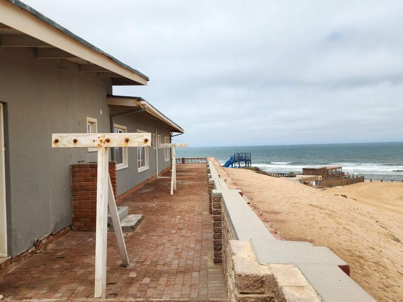 Rear exterior patio area featuring brick paving and a retaining wall, offering direct views of the adjacent beach and coastline.