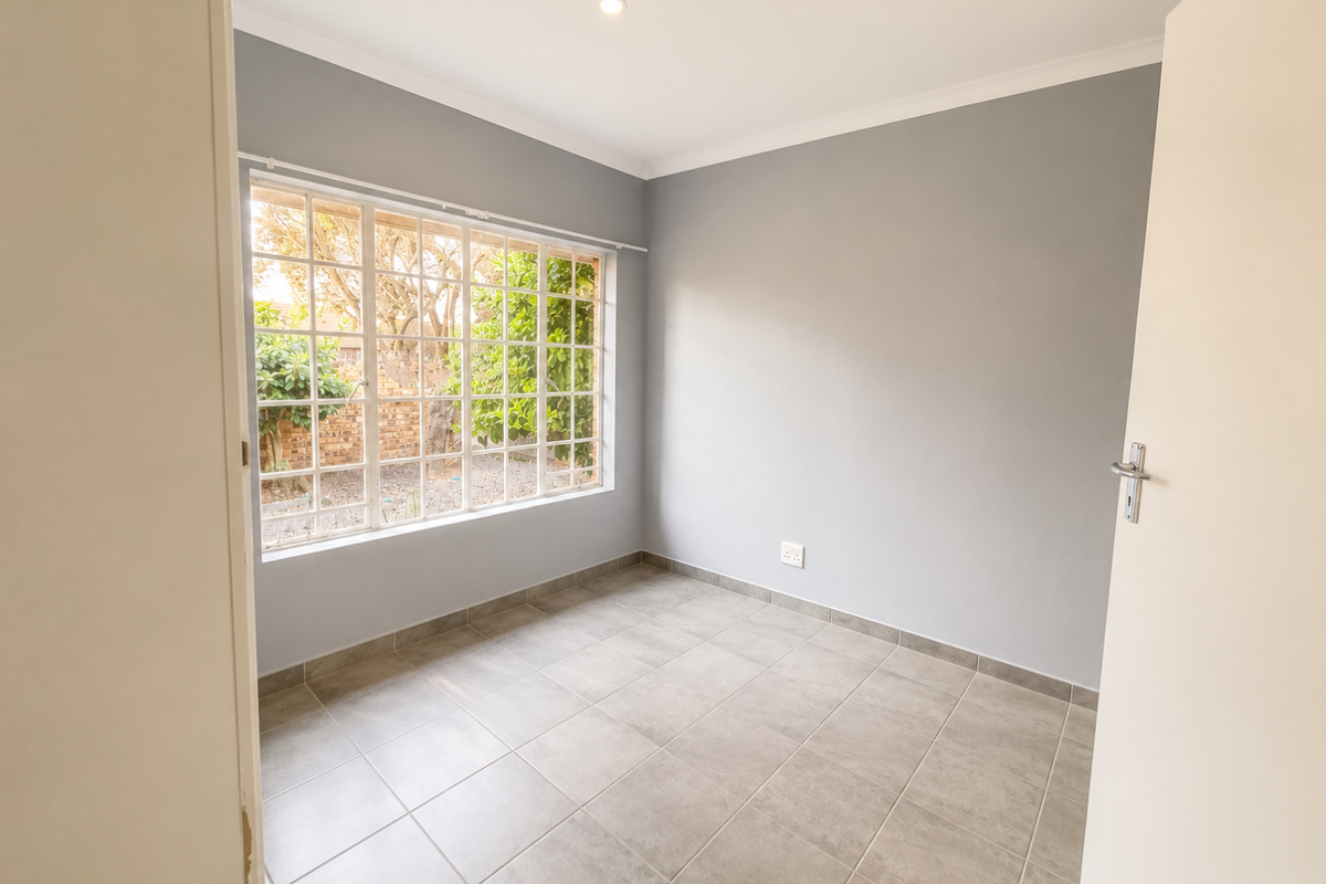 A bright, empty bedroom featuring neutral grey walls, large grid-pattern windows, and modern tiled flooring, offering a clean canvas for personalization.