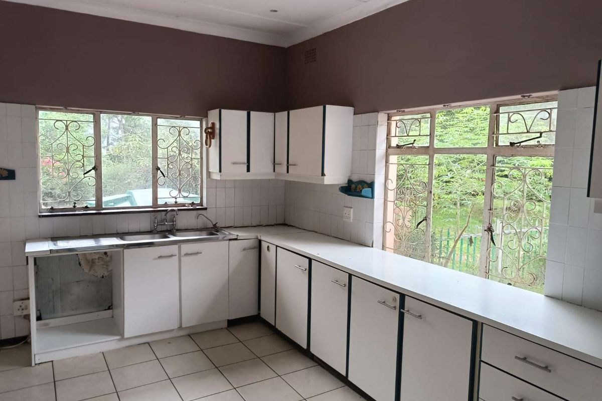 A dated kitchen featuring white cabinetry, tiled countertops, and large windows with security bars, offering a functional layout with potential for modernization.