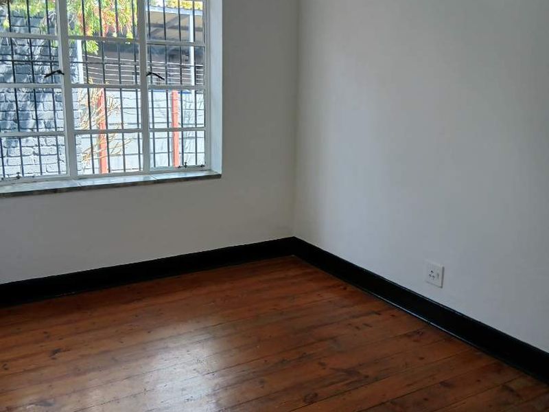 A vacant bedroom featuring original timber flooring, steel-framed windows with security bars, and dark-painted skirting boards.