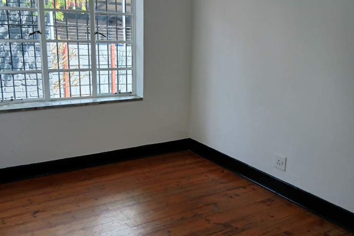 A vacant bedroom featuring original timber flooring, steel-framed windows with security bars, and dark-painted skirting boards.