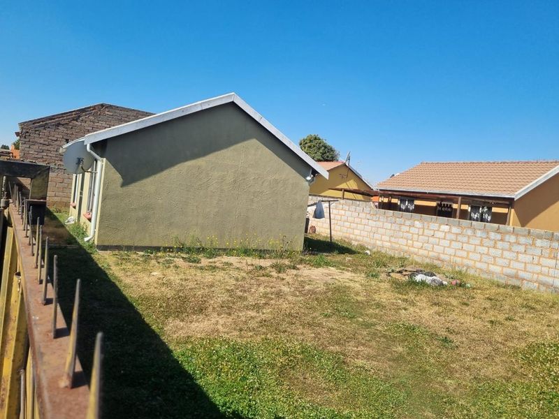 Rear exterior view of the property featuring a grass yard, perimeter wall, and metal fencing.