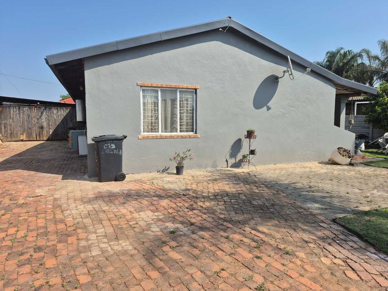 Rear exterior view of the property featuring a brick paved driveway and a grey rendered facade with security bars on the window.