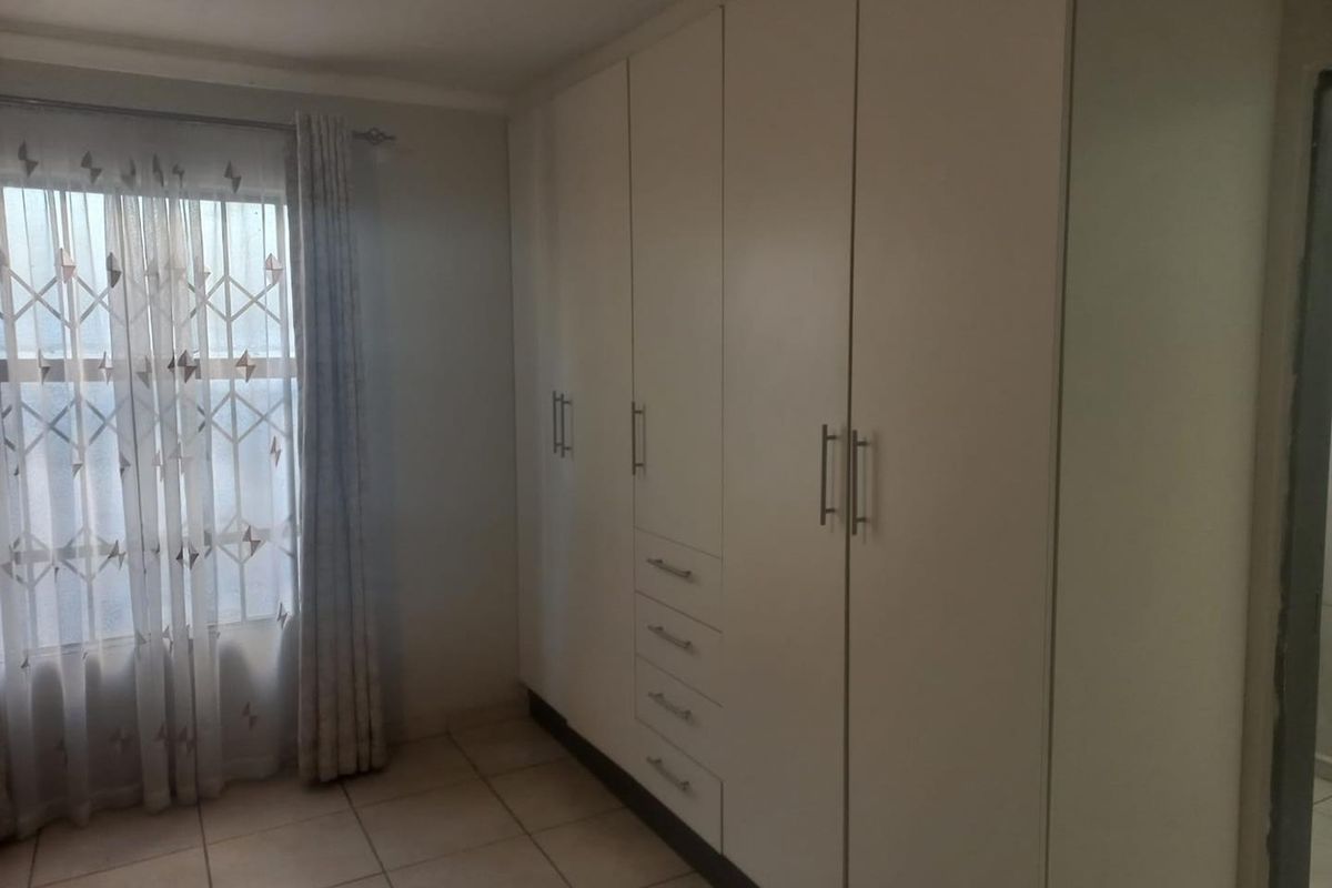 A clean, empty bedroom featuring neutral tiled flooring and extensive white built-in cupboards with integrated drawers.