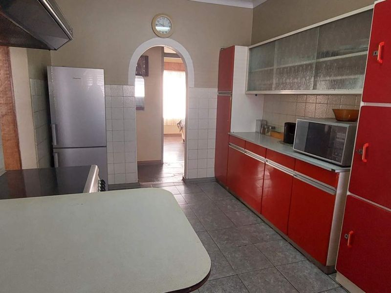 A functional kitchen featuring retro red cabinetry, tiled splashbacks, and an arched doorway leading to the adjacent living space.