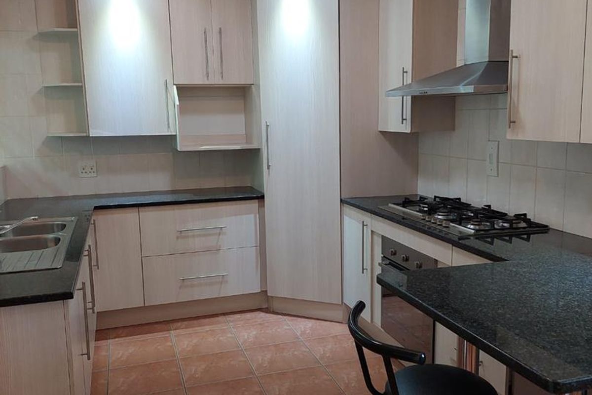 A functional kitchen featuring light wood cabinetry, granite countertops, a gas hob, stainless steel extractor fan, and tiled flooring.