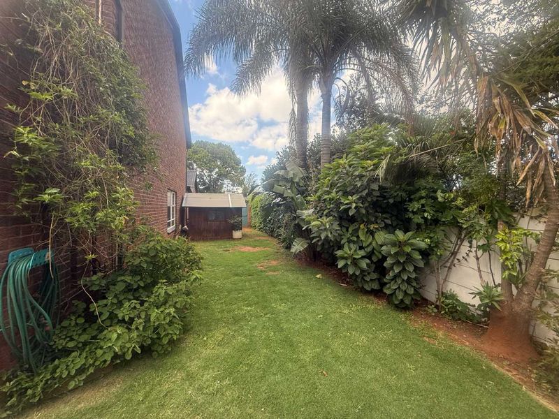 A side garden area featuring a brick townhouse exterior, a small storage shed, and established garden landscaping.