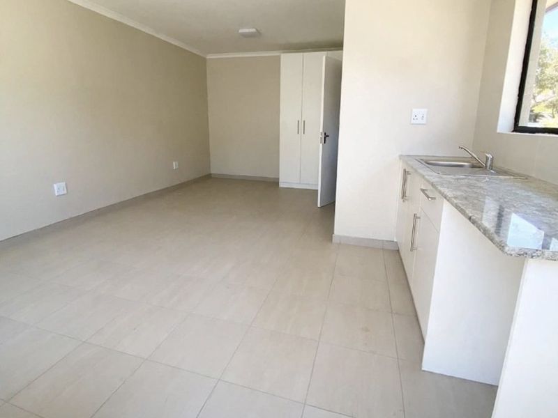 An open-plan living area featuring tiled flooring, built-in cupboards, and a compact kitchenette with a granite countertop and sink.