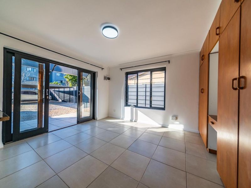 A bright, empty bedroom featuring tiled floors, built-in wooden cupboards, and sliding glass doors providing direct access to an outdoor area.