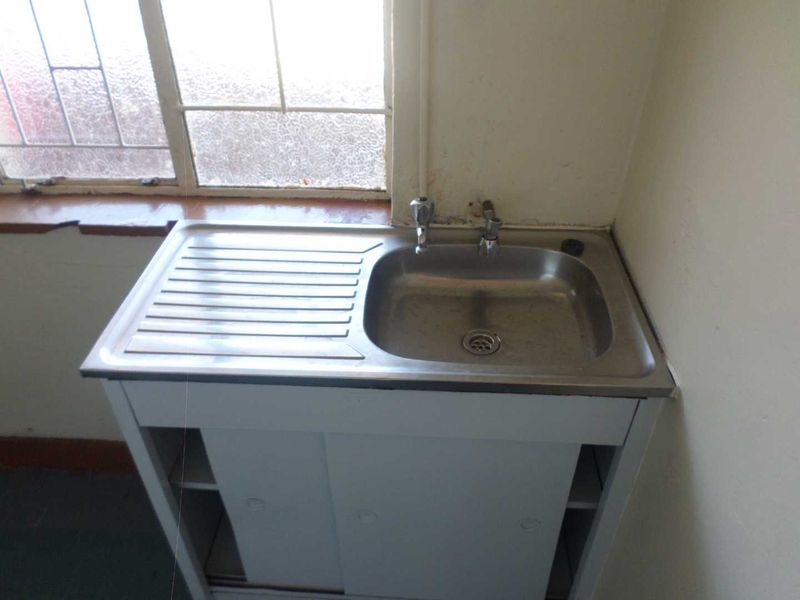 A functional laundry area featuring a stainless steel sink with a drainer board and built-in cabinetry, situated beneath a window.