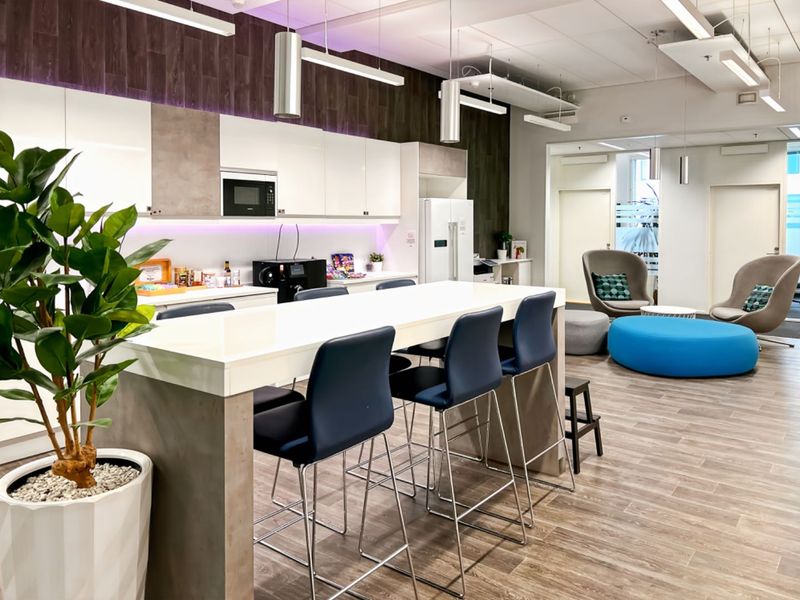 Modern open-plan office kitchen and breakout area featuring sleek cabinetry, integrated appliances, contemporary lighting, and durable wood-look flooring.