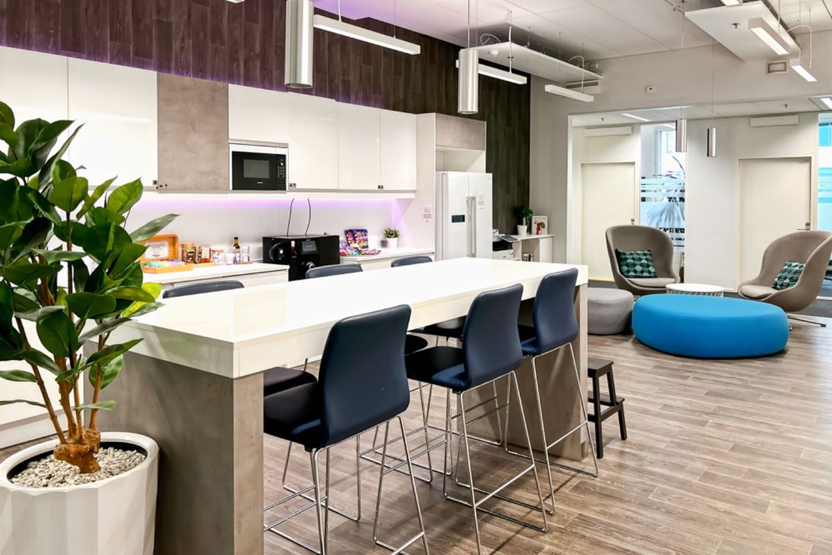 Modern open-plan office kitchen and breakout area featuring sleek cabinetry, integrated appliances, contemporary lighting, and durable wood-look flooring.
