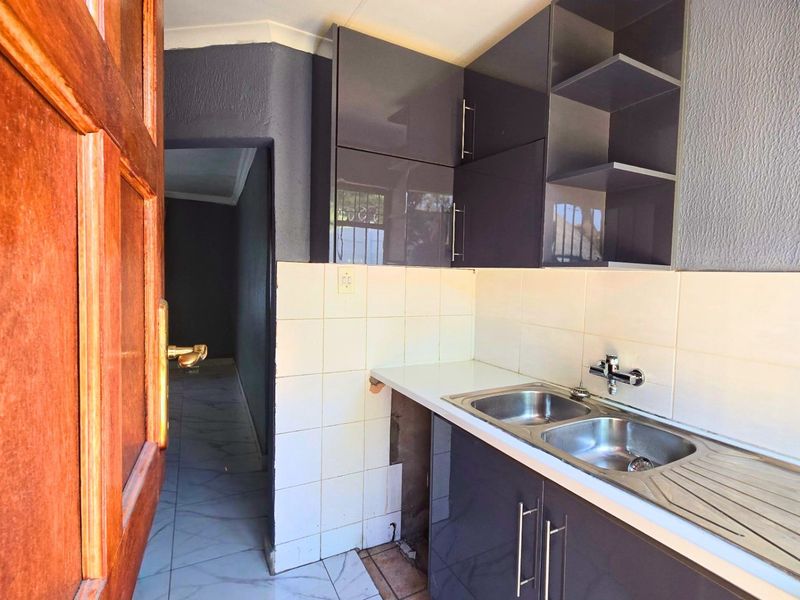 A compact scullery area featuring dark grey cabinetry, a double bowl stainless steel sink, and tiled splashbacks, requiring minor finishing work to the cabinetry base.