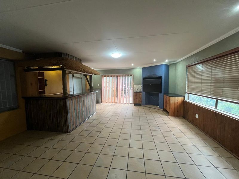 Spacious entertainment area featuring a built-in thatched bar, fireplace, tiled flooring, and sliding door access to the exterior.