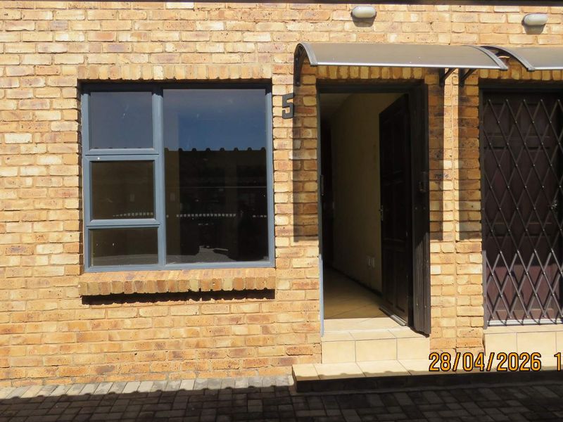 Front entrance of the apartment featuring a face brick facade, aluminium window frames, and a secure entrance door with an overhead awning.