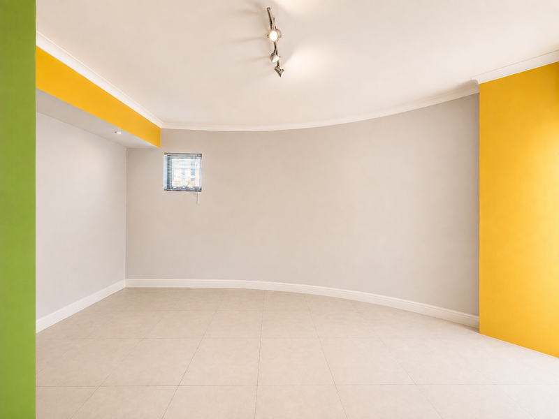 A bright, empty living area featuring neutral tiled flooring, a distinctive curved wall, and modern track lighting.