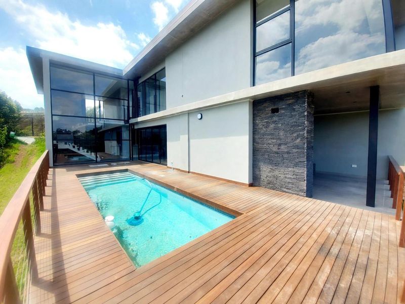 Modern outdoor pool area featuring extensive timber decking, a stone-clad feature wall, and large glass windows overlooking the swimming pool.