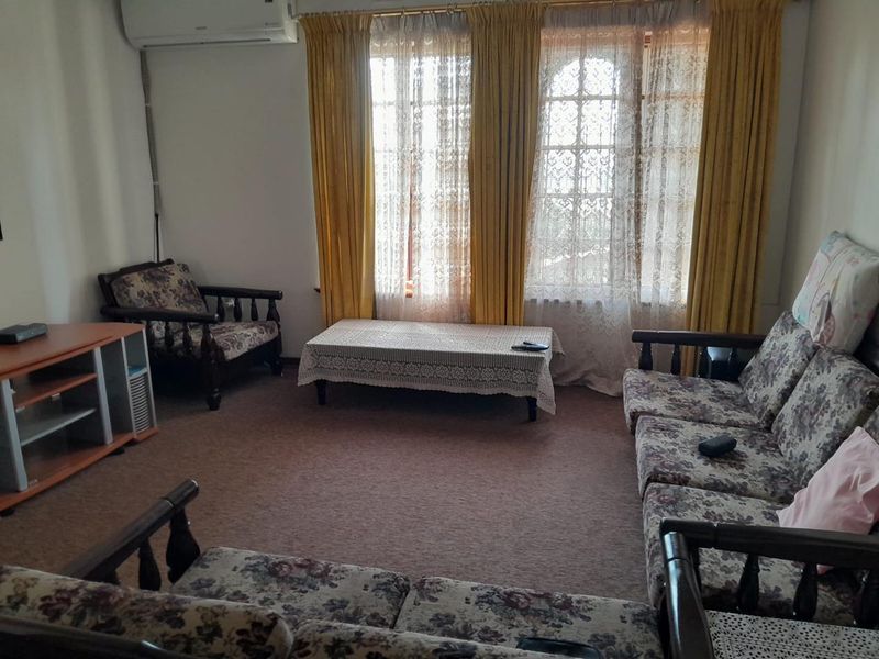 A living room featuring arched windows and a wall-mounted air conditioning unit, with carpeted flooring throughout.
