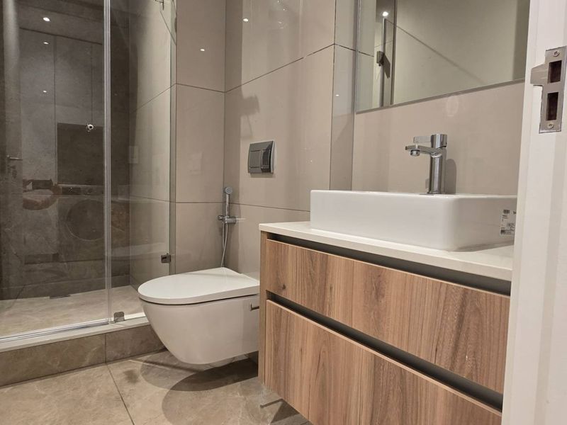 Modern bathroom featuring a wall-hung toilet, glass shower enclosure, and a contemporary vanity with a vessel sink and wood-finish cabinetry.