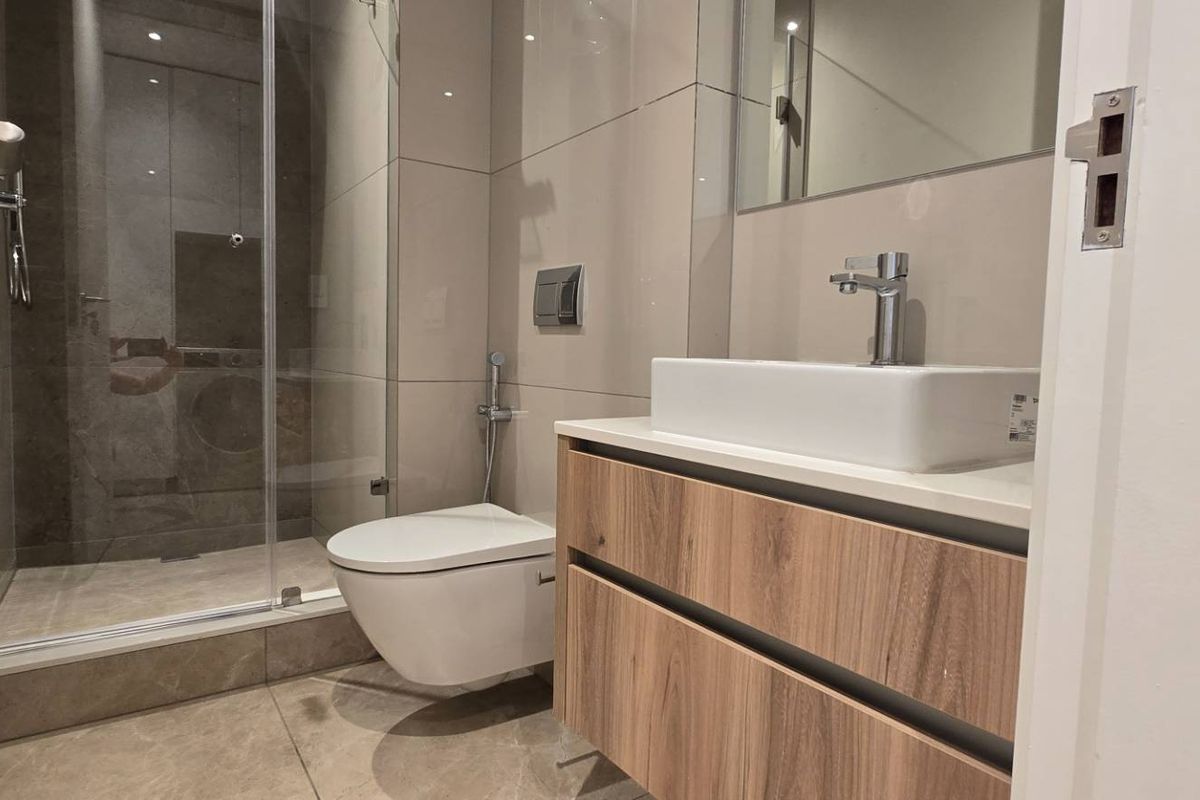 Modern bathroom featuring a wall-hung toilet, glass shower enclosure, and a contemporary vanity with a vessel sink and wood-finish cabinetry.