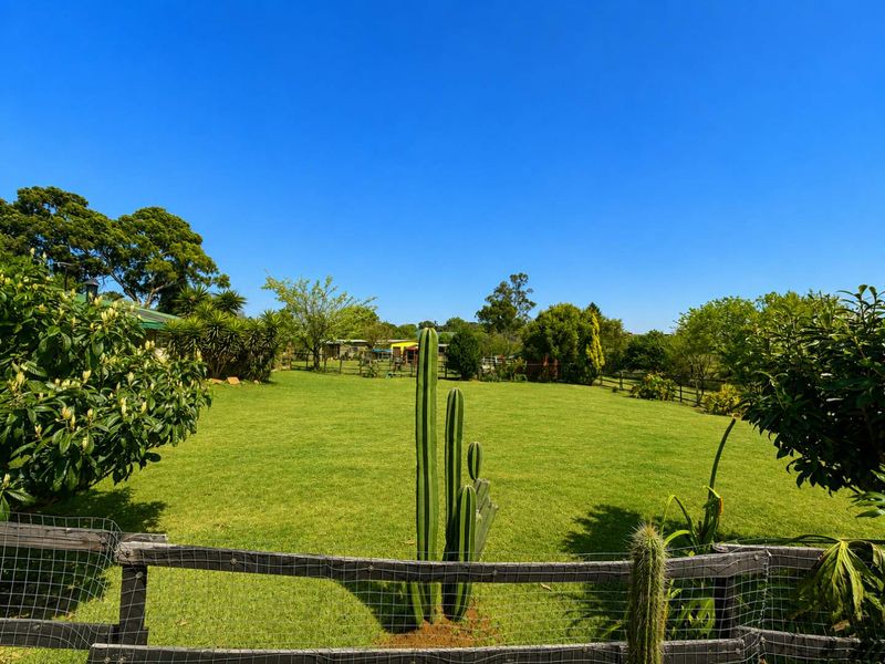A well-maintained, expansive green lawn area enclosed by a wire mesh and wooden post fence, featuring mature trees and shrubs.