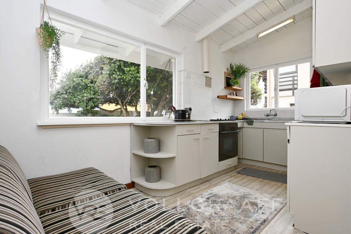 Compact kitchen featuring built-in cabinetry, integrated oven and hob, and large windows providing natural light and garden views.