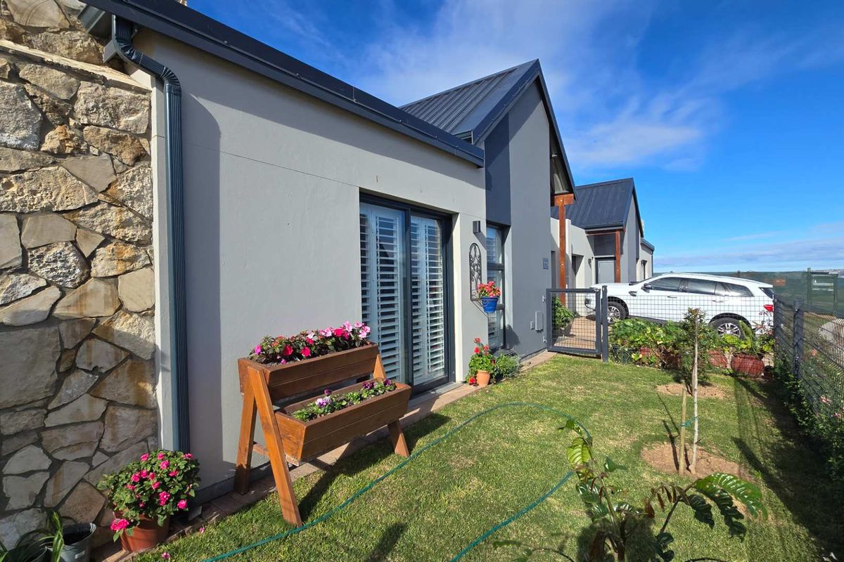 A well-maintained rear exterior view featuring modern stone cladding, dark metal roofing, and sliding glass doors opening onto a landscaped garden area.