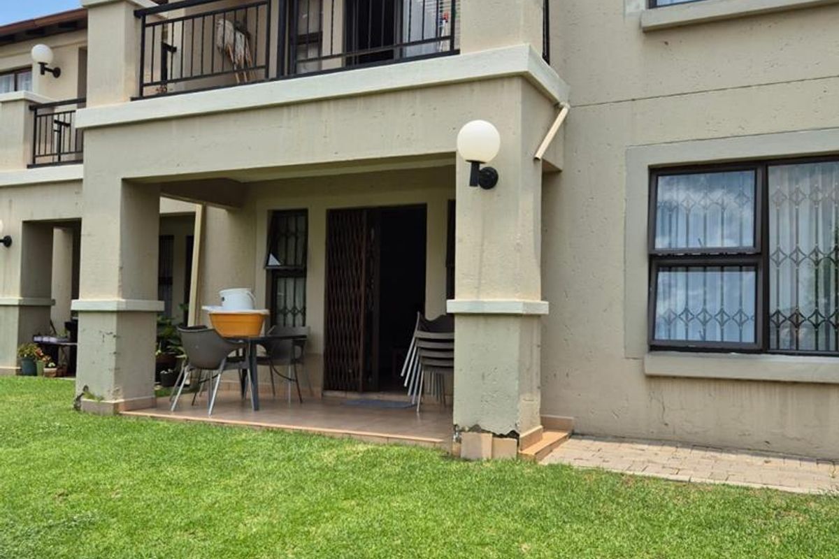Rear view of the townhouse featuring a ground floor patio, upper balcony with metal railings, and access to a private garden area.