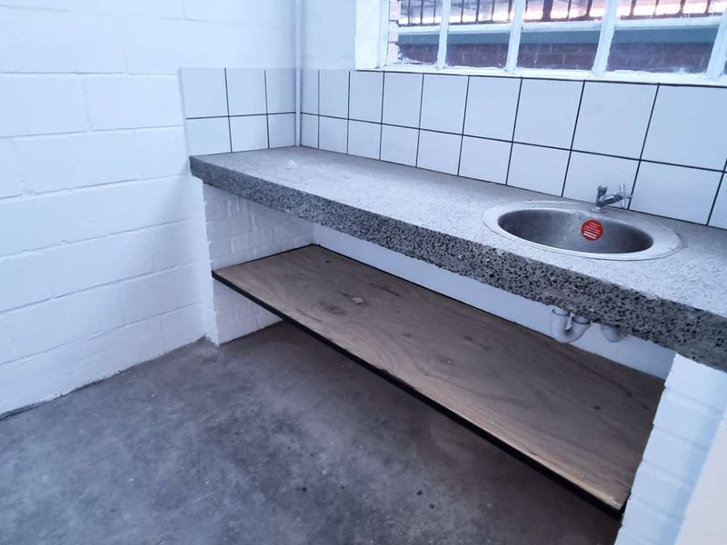 A functional industrial-style scullery or utility area featuring a concrete countertop, integrated sink, tiled splashback, and open timber shelving.