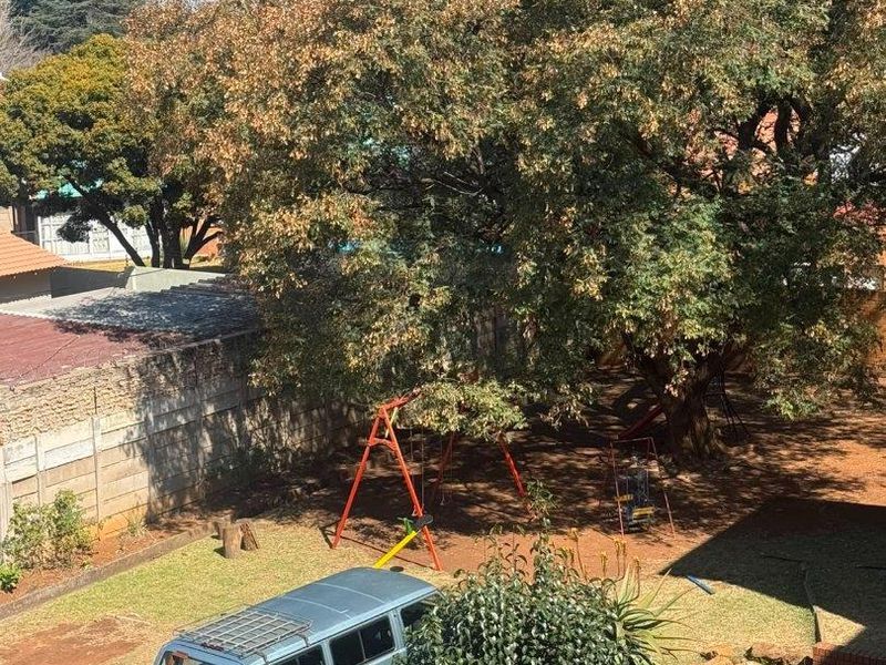 An elevated view of a rear garden area featuring a large mature tree and a precast concrete boundary wall.