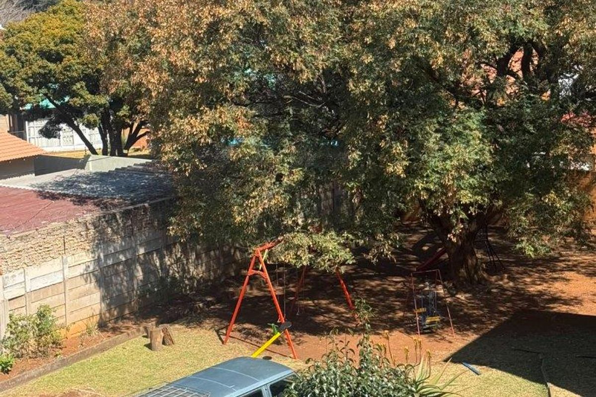 An elevated view of a rear garden area featuring a large mature tree and a precast concrete boundary wall.