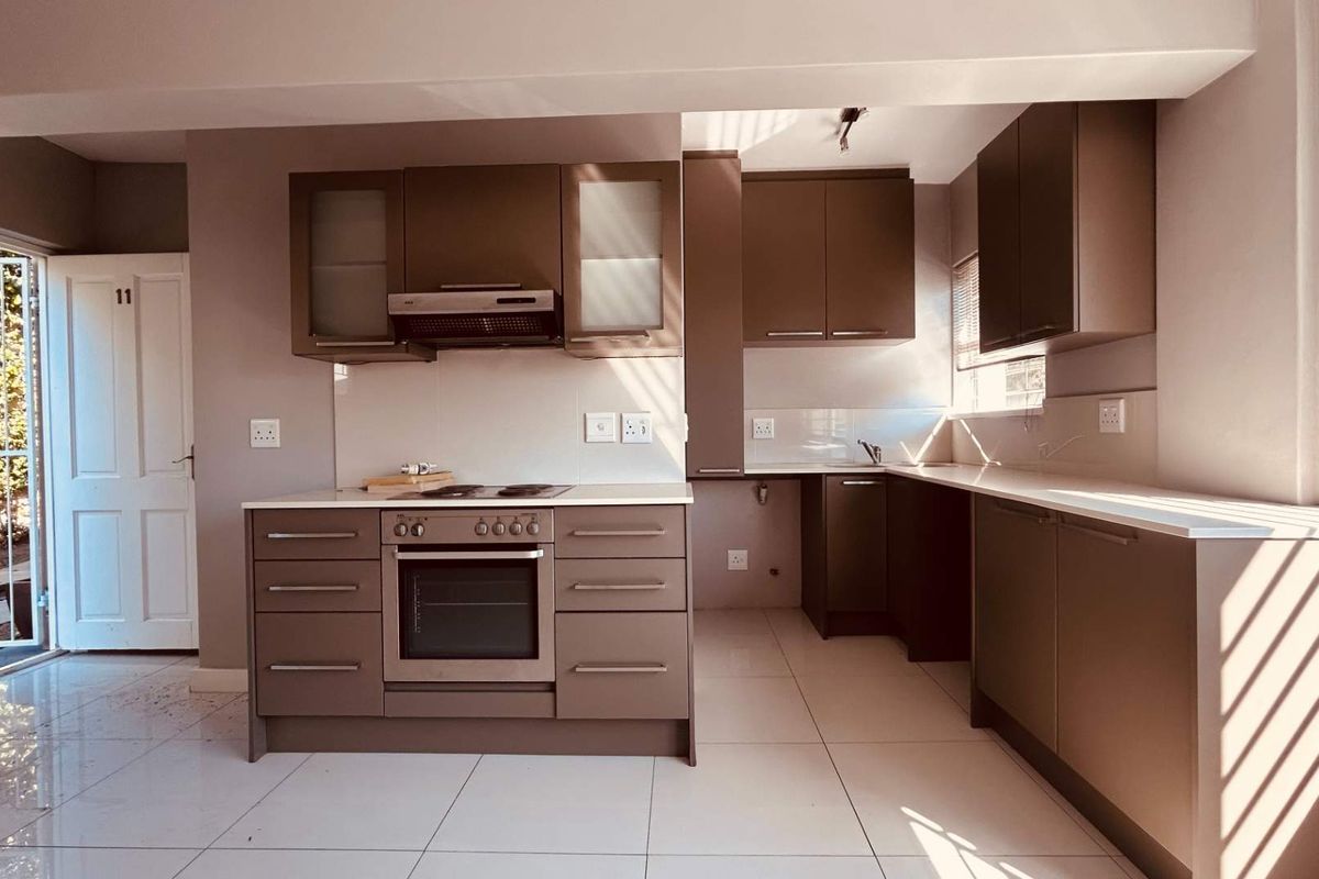 Modern kitchen featuring dark cabinetry, built-in oven and hob, light countertops, and tiled flooring with direct access to an outdoor area.