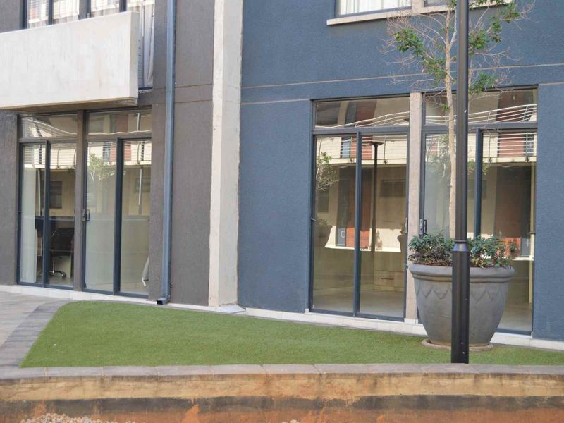 Ground floor apartment exterior featuring sliding glass doors, a small artificial turf area, and a concrete retaining wall.