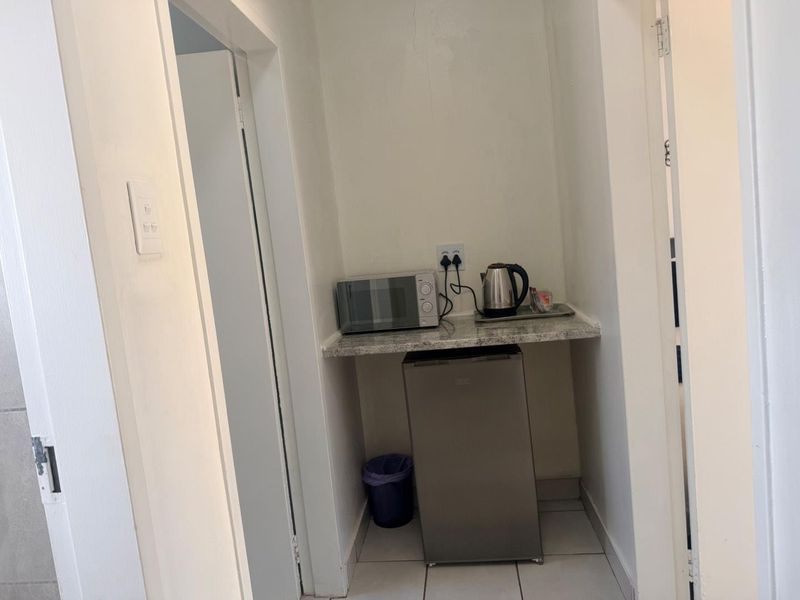 A compact scullery or kitchenette area featuring a granite countertop, tiled flooring, and dedicated electrical points for small appliances.