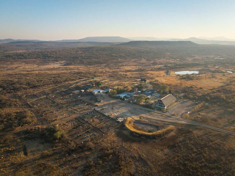 Aerial view of a large rural property featuring multiple farm buildings, extensive livestock enclosures, and surrounding natural landscape.