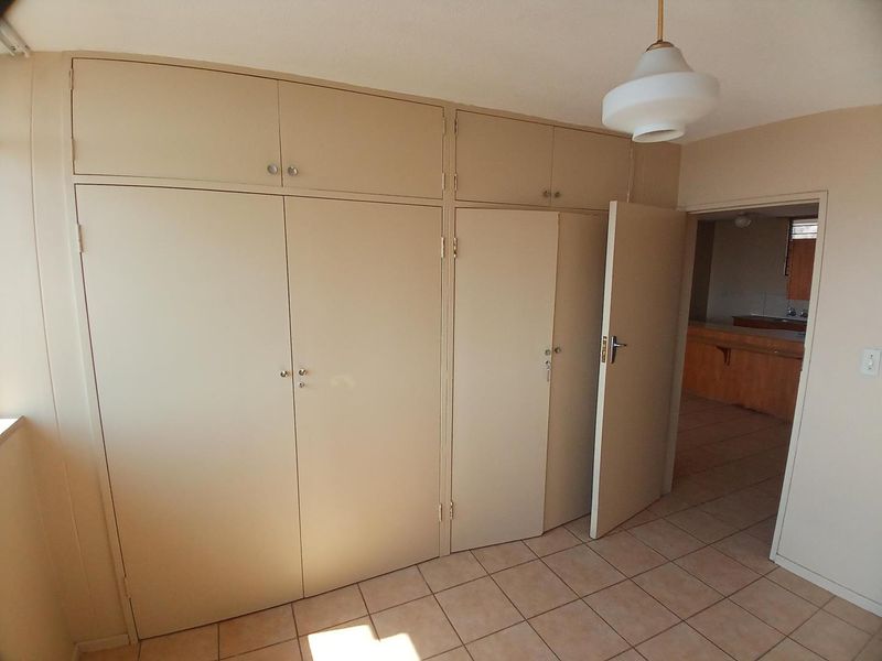 A bedroom featuring neutral tiled flooring and extensive built-in cupboard storage, offering a clean and functional space ready for personalization.