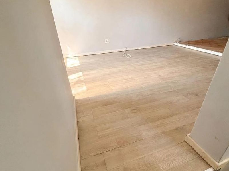 An empty living area featuring light-toned laminate flooring and neutral walls, currently awaiting final finishing touches and trim work.
