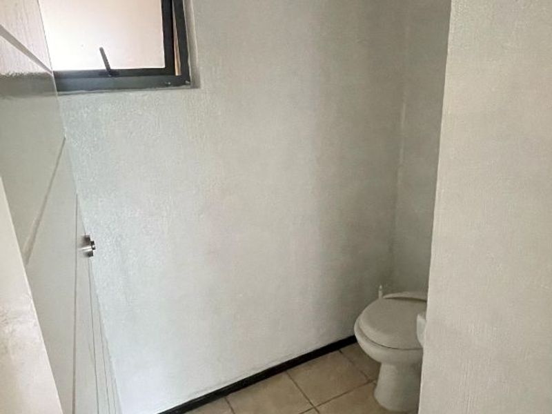 A compact, empty bathroom featuring tiled flooring, a standard toilet, and a top-hung window, requiring cosmetic updates to improve its overall condition.