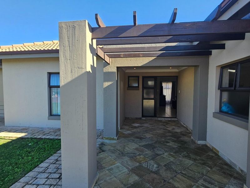A covered patio area featuring stone paving, a timber pergola structure, and direct access to the interior through sliding glass doors.
