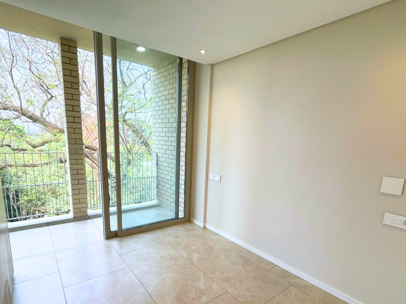 A bright, empty bedroom featuring modern tiled flooring, recessed lighting, and a sliding glass door leading to a private balcony.