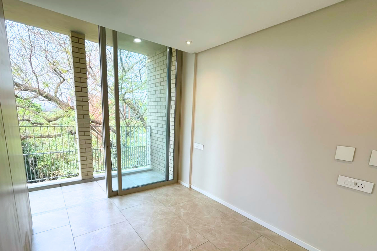 A bright, empty bedroom featuring modern tiled flooring, recessed lighting, and a sliding glass door leading to a private balcony.