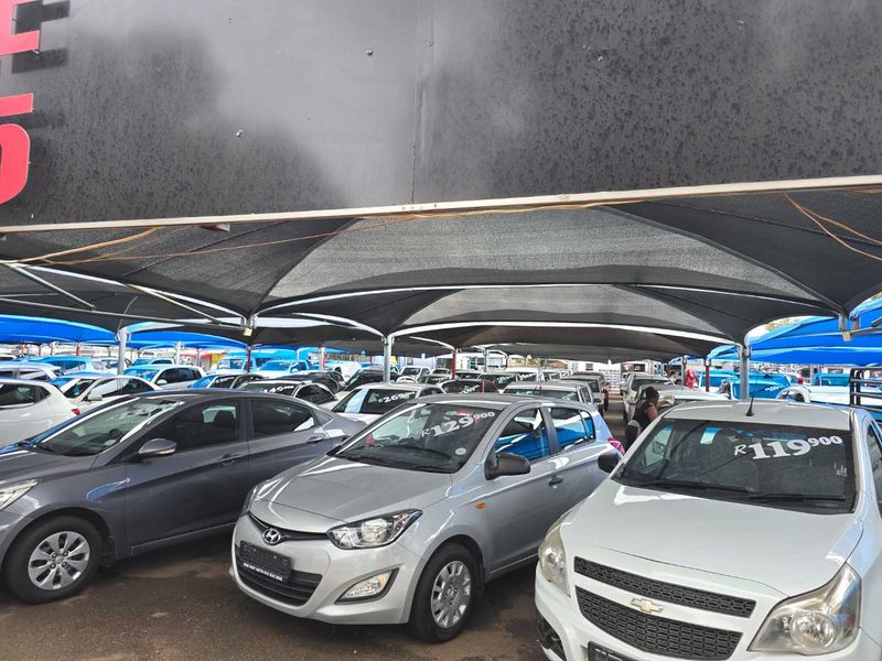 A commercial vehicle display area featuring a large shade cloth canopy structure over a paved lot.