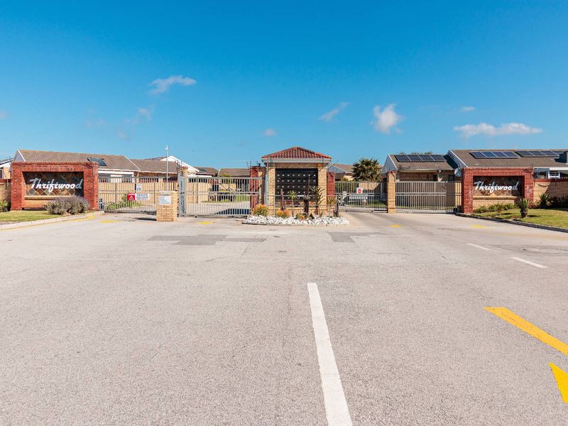 The secure entrance to Thriftwood complex featuring brick signage walls, metal security gates, and a central gatehouse with integrated post boxes.