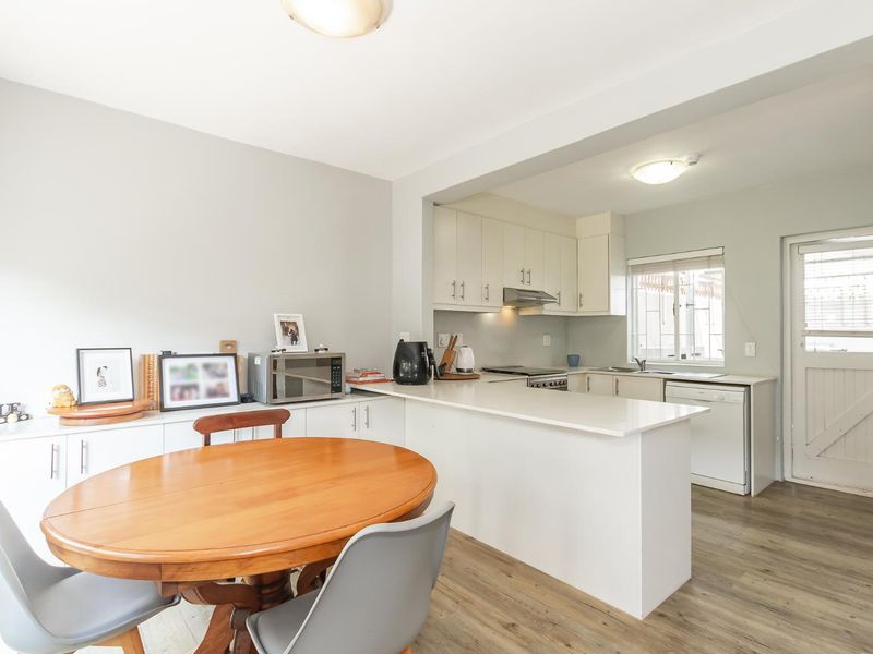 Open-plan kitchen and dining area featuring white cabinetry, stone countertops, stainless steel appliances, and durable laminate flooring with direct access to the exterior.