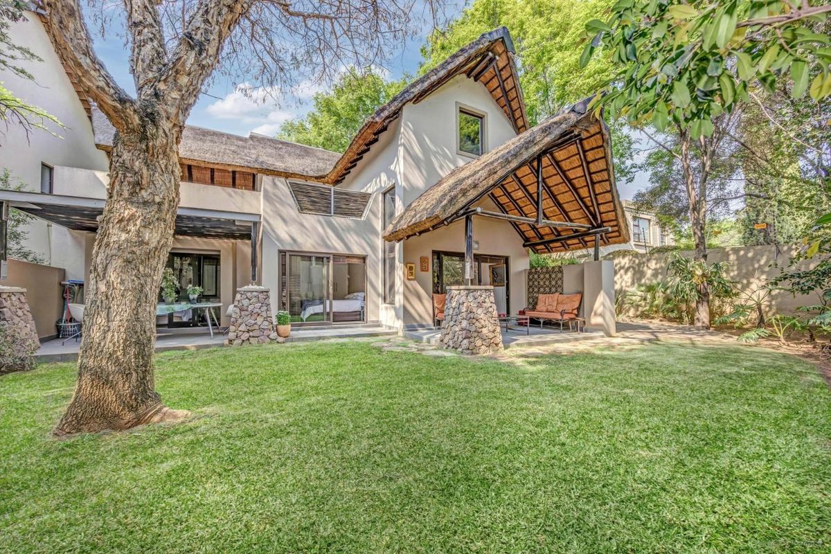 Rear view of a cluster home featuring a thatched roof, stone-clad pillars, a covered patio area, and a well-maintained garden.