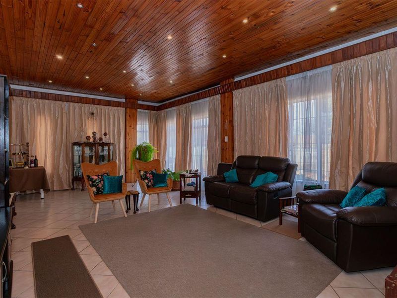 Spacious living room featuring warm timber tongue and groove ceilings, recessed lighting, and tiled flooring, creating a cozy and traditional atmosphere.