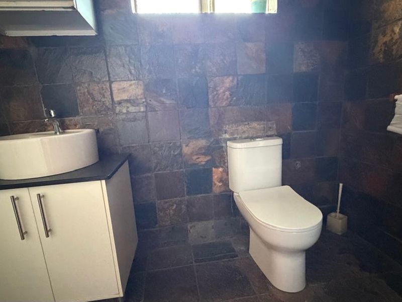 A bathroom featuring dark slate wall and floor tiles, a white vanity cabinet with a vessel sink, and a modern toilet.
