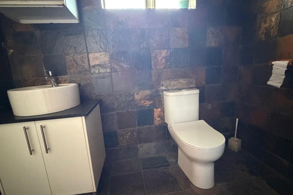 A bathroom featuring dark slate wall and floor tiles, a white vanity cabinet with a vessel sink, and a modern toilet.
